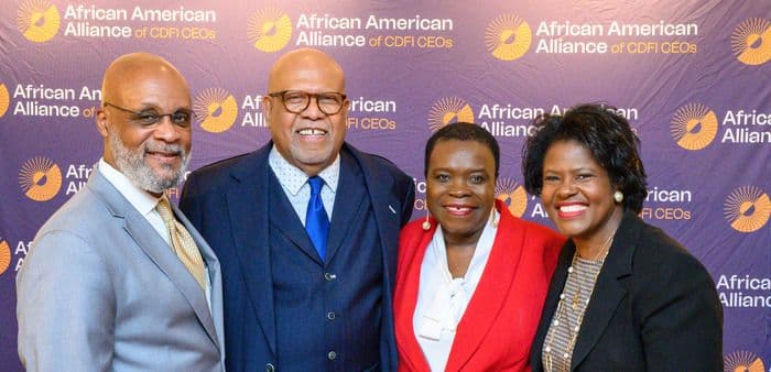 Four smiling professionals, two men and two women, pose at an African American Alliance event.