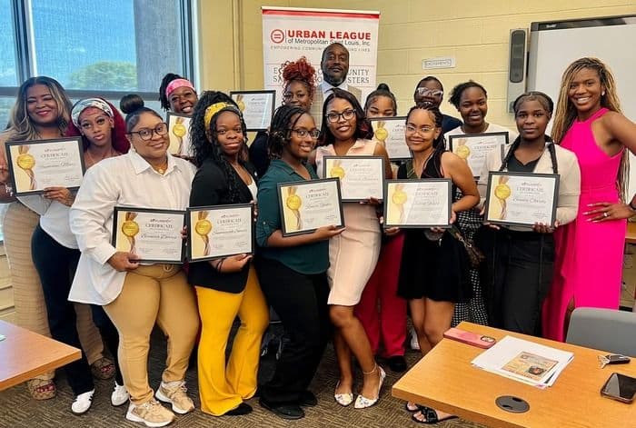 Diverse group of women and one man proudly holding certificates at an Urban League event.