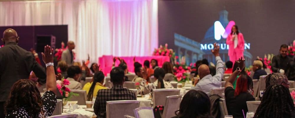 Audience with raised hands at an event featuring a speaker on stage with a 'MOTION' logo.