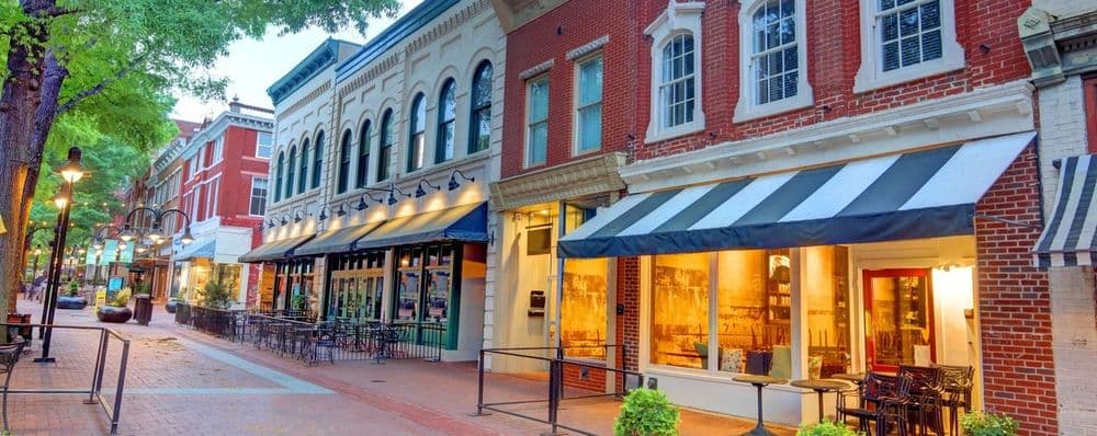 A vibrant downtown street at dusk, lined with historic buildings, awnings, and outdoor dining areas.