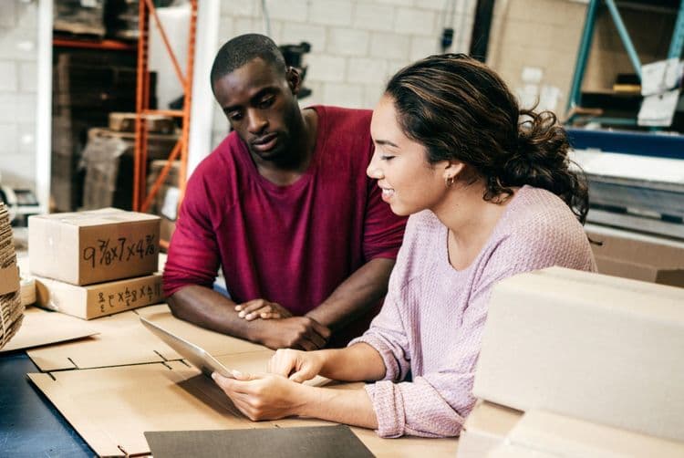 A man and woman review paperwork in a professional warehouse setting.