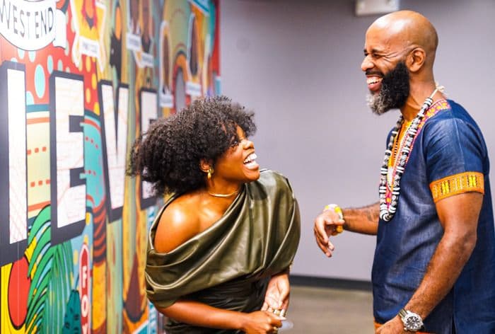 Black woman and man laughing happily by a colorful mural wall.