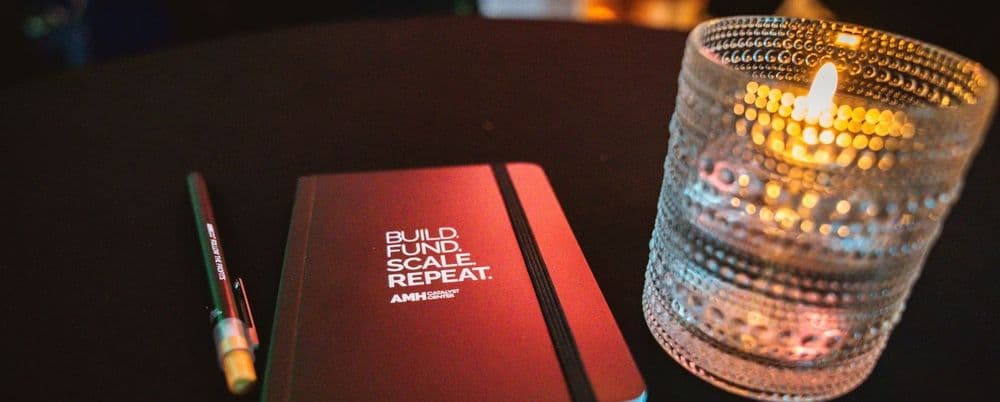 A red notebook with "BUILD. LEAD. SCALE. REPEAT." next to a pen and a lit candle.