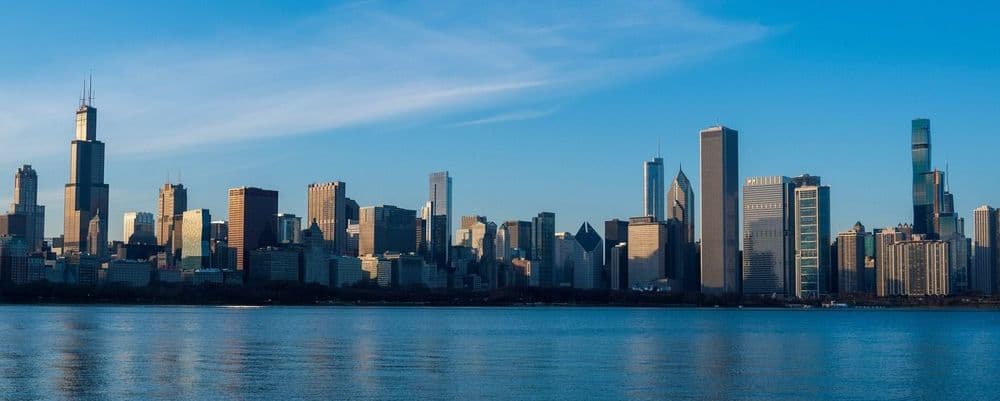 Panoramic city skyline of tall buildings across a wide body of water.