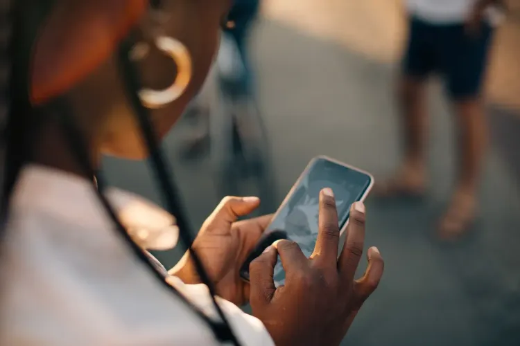 A person with braids and a hoop earring is actively using a smartphone outdoors.
