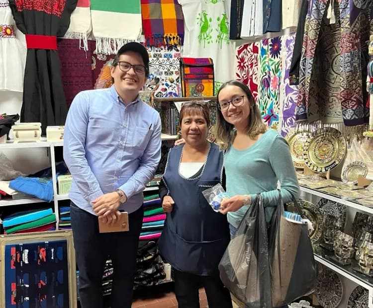Three people smiling in a vibrant shop filled with traditional crafts and embroidered textiles.