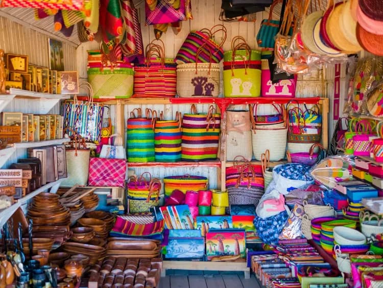 A vibrant market stall overflows with colorful, handcrafted woven baskets, bags, and decorative containers.